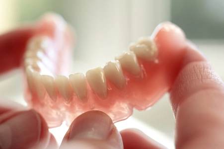 Closeup of a hand holding a bottom set of dentures. 